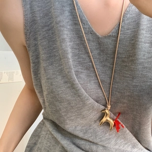 Pony pendant necklace with gold body and red tail on a minimal beige cord