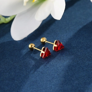 Macro detail of triangle screw-back earrings with red gemstones in golden settings