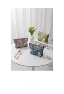 Close-up of three floral jacquard makeup bags in purple, blue and green with gold thread