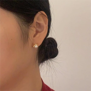 Close-up of elegant gold bow earrings with a white round pearl drop on a female model