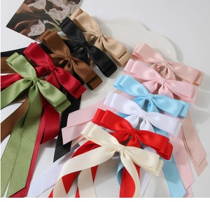 Flat lay of multiple colorful satin bow hair clips with long ribbons on a white tray