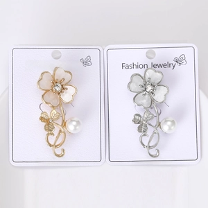 Detail shot of golden and silver clover brooches with opal petals and pearl pendants