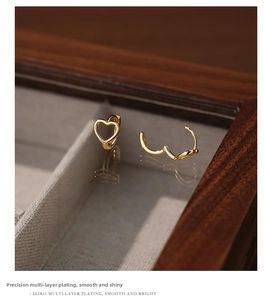 Detailed close-up of hollow heart-shaped gold plated earrings on a luxury wooden jewelry box