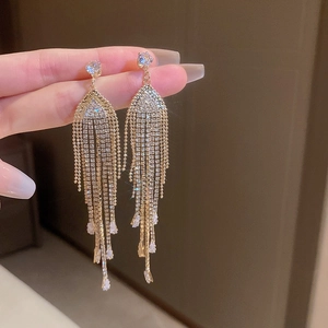 Macro detail of long golden tassel earrings featuring sparkling crystal rhinestones on the hand