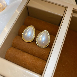 Detailed view of teardrop pearl earrings with golden engraved edges on velvet