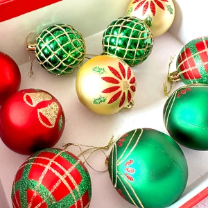 Close-up of red and green Christmas ball ornaments with glitter patterns in a white box