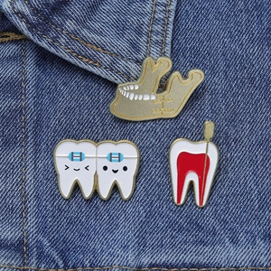 Detailed dental enamel pins featuring root canal and braces on blue denim fabric background
