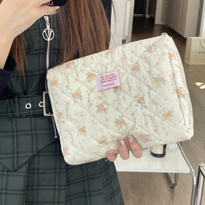 Close-up of floral quilted cosmetic bag with pink label and metal zipper closure