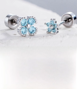 Macro detail of silver cartilage studs with light blue zircon in clover and star shapes