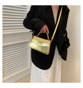 Détail d'un mini sac doré avec relief de nœud et fine bandoulière métallique chic