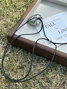 Detail of engraved heart pendant on black cord necklace set on a rustic wooden tray