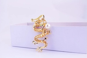 Detailed view of a golden dragon brooch with intricate scales and a white pearl accent