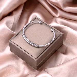 Macro shot of silver metal bangle featuring a central spiral knot and ball end details