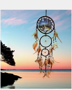 Detail of dream catcher with wolf print, red beads and natural feathers against sunset