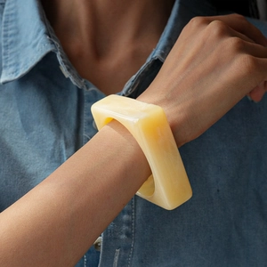 Close-up of a wide square acrylic bangle with yellow marble texture on denim sleeve