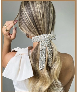 Detail of beige fabric bow hair clip with silver crystal rhinestones worn by a model