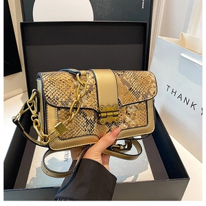 Detailed view of snake skin crossbody bag with gold chain and bow metal clasp on gift box