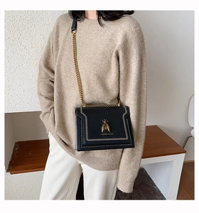 Close-up of black crossbody bag with golden bee buckle and fine chain strap detail