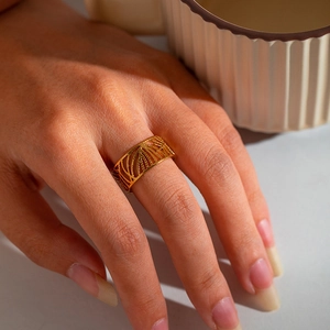 Detail of gold-plated stainless steel ring with hollow leaf texture on a model's hand