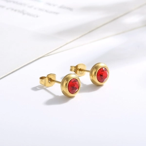 Macro view of gold-plated titanium steel stud earrings featuring red round-cut crystals