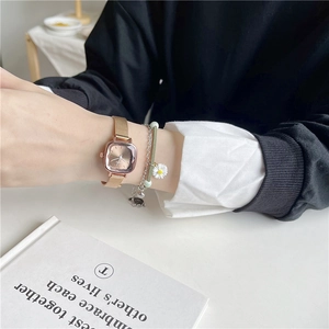 Detail of rose gold square watch with green daisy bracelet on model wrist