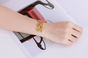 Detail of adjustable gold bangle featuring round love charms on model wrist