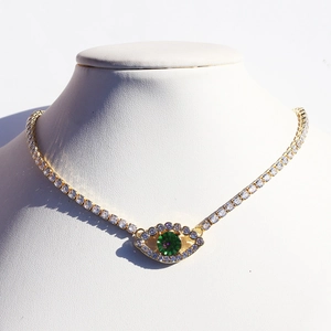 Macro detail of gold devil eye necklace with green and white zircons on a white bust