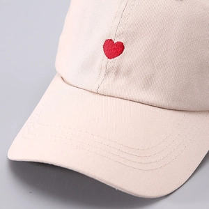 Close-up of red heart embroidery on a light beige cotton baseball cap with fine stitching