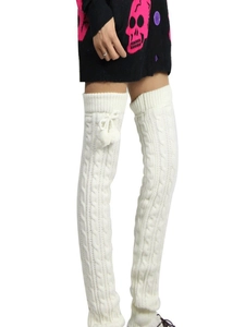 Detail of white cable knit leg warmers featuring plush pom-poms and ribbon bows