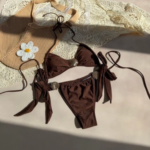 Flat lay of brown bikini with gold shell hardware, sunhat, and daisy on a textured surface