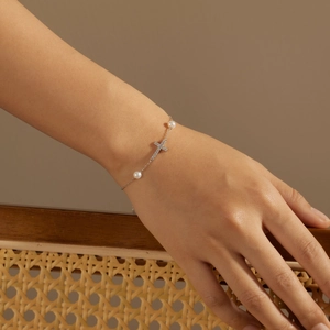 Detailed close-up of a silver cross bracelet with central zircon and two white pearls