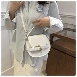 Detail view of a white minimalist saddle bag worn by a model in a bright indoor setting