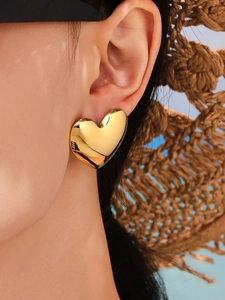 Close-up of polished gold heart stud earring on model with summer straw hat background