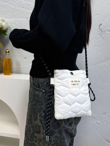 Detailed view of white quilted mini crossbody bag with chic polka dot woven strap and glossy texture