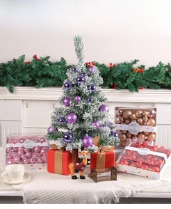 Detailansicht eines beschneiten Weihnachtsbaums mit lila Kugeln und festlichen Geschenkboxen