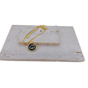 Gold plated necklace featuring a round black enamel snake pendant on a stone slab