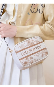 Detail of a beige canvas crossbody bag with floral prints and a LUCK FOR YOU strap
