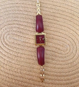 Close-up of a square gold watch with a burgundy dial and a leather chain strap