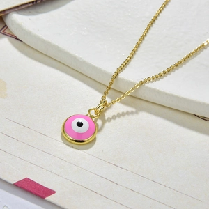 Detail of pink Evil Eye pendant with gold plating on a textured white surface