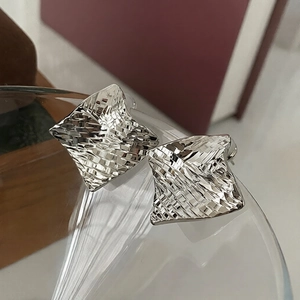 Macro detail of silver geometric square earrings with textured woven metal surface