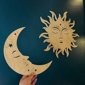 Detail of wooden sun and moon wall decor in light plywood finish held against dark wall