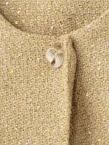 Detail of tweed fabric with gold sequins and textured metal button on the jacket