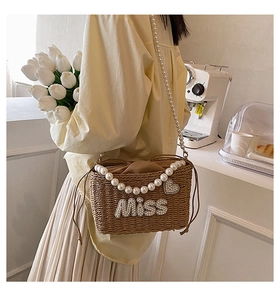 Detail of woven straw bucket bag featuring pearl Miss letters and a heart charm