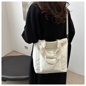 Minimalist beige canvas tote bag shown as a shoulder bag on a model in a black coat