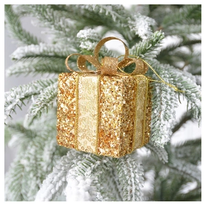 Macro shot of gold sequin Christmas gift box ornament hanging on a snowy pine branch