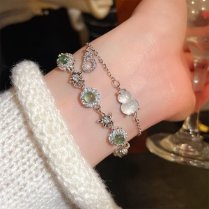 Detail of silver layered bracelets with green gemstones and white gourd-shaped charm