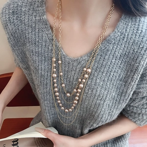 Detail view of multi-layered pearl necklace on a grey sweater with golden chain accents