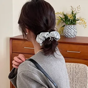 Detail of silver metallic scrunchie with pleated texture on a low ponytail hairstyle