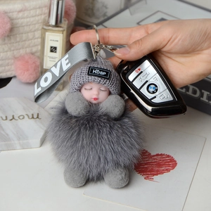 Detailed view of gray fox fur pompom with a sleeping doll charm and LOVE ribbon keychain