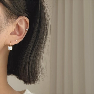 Close-up of heart-shaped zircon earrings with gold hooks worn in a layered style